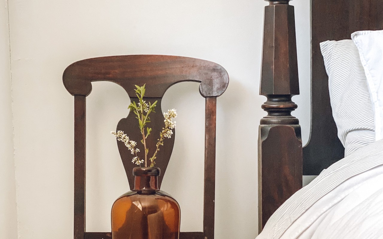 vintage wooden chair with amber colored vase sitting on top with small white flowers in it.